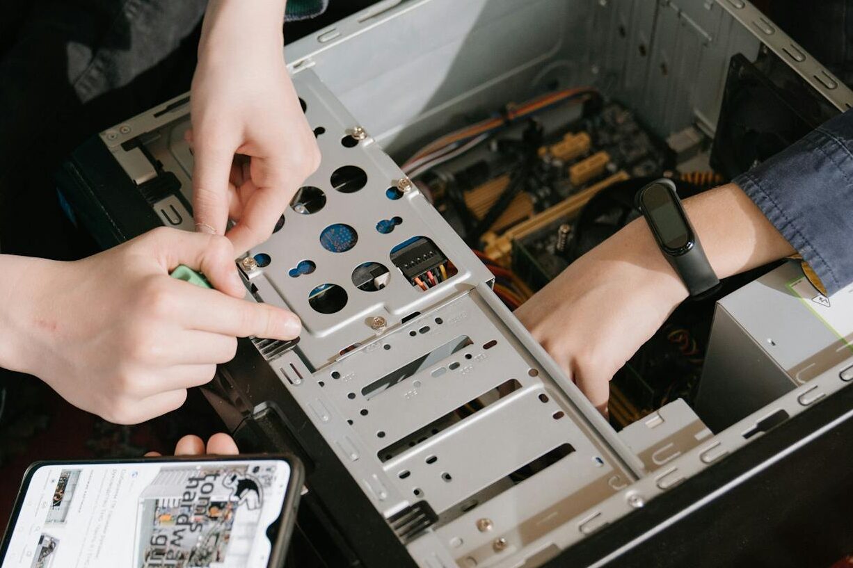 A close-up of hands fixing a computer with guidance from a mobile device.